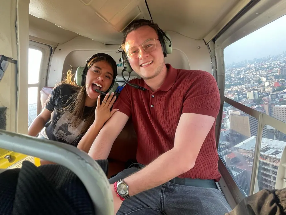 Pareja sonriendo dentro de la cabina de un helicóptero de HeliStar, con la ciudad al fondo
